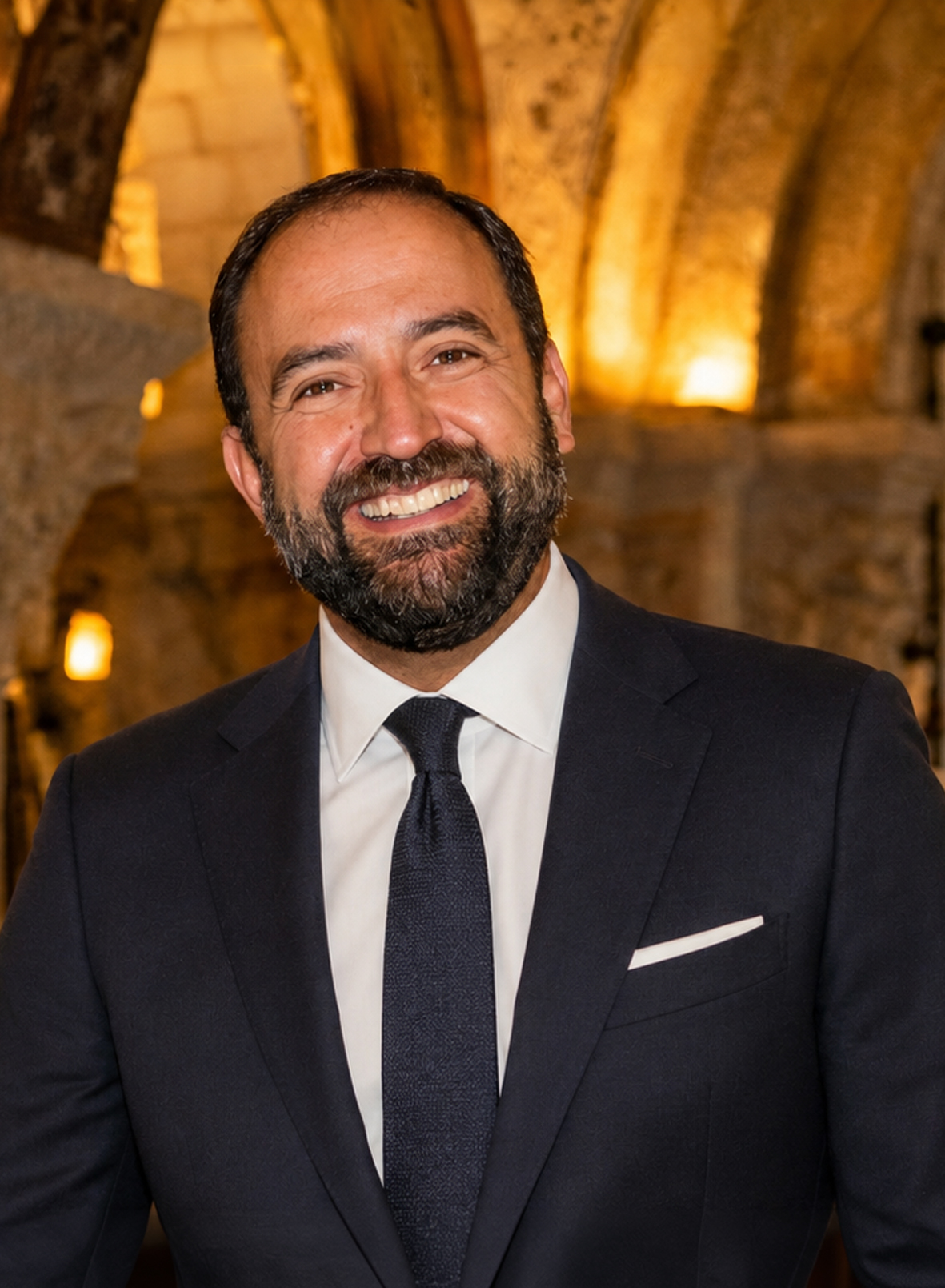 Retrato de José Miguel Ortega del Río, historiador del arte y escritor, sonriente y con traje oscuro ante unas bóvedas de piedra iluminadas